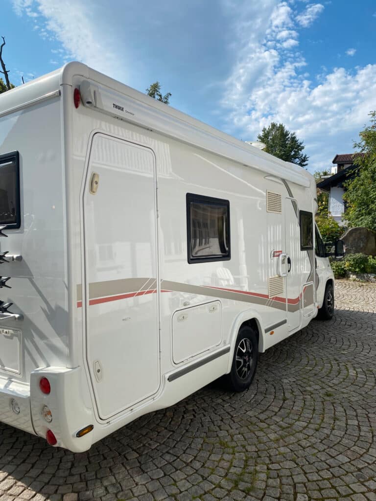 Camping-car blanc stationné sur pavé sous ciel bleu.
