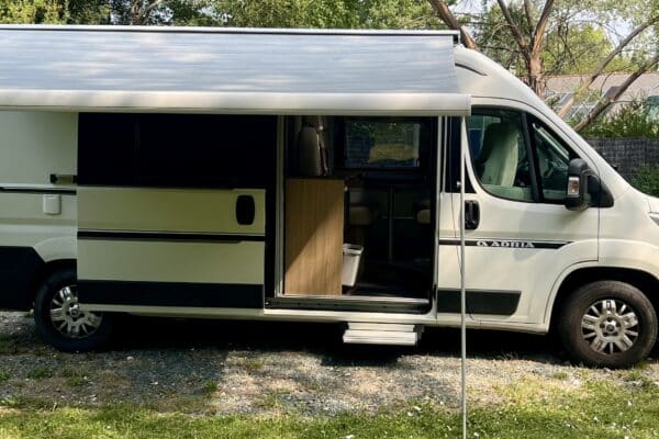 Wohnmobil mit ausgefahrenem Vordach in einem grünen Garten.