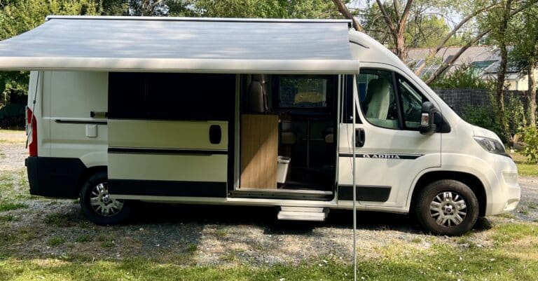 Camping-car avec auvent déployé dans un jardin verdoyant.