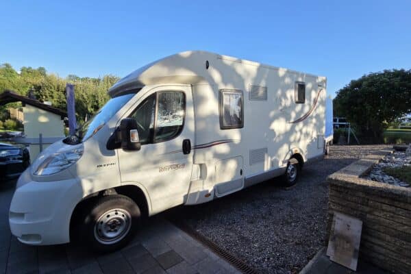 Camping-car blanc stationné sur allée pavée.