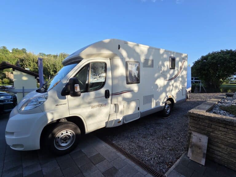 Camping-car blanc stationné sur allée pavée.