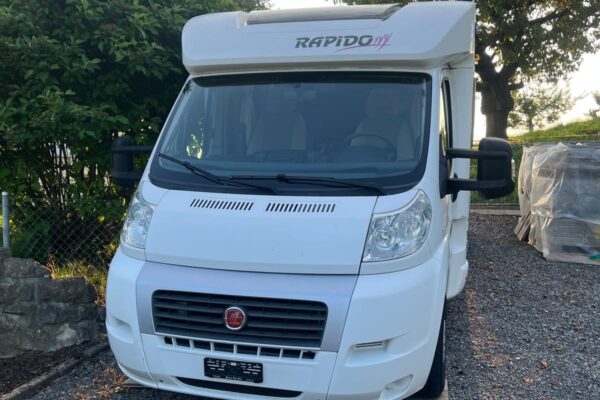 Camping-car blanc garé sur gravier.