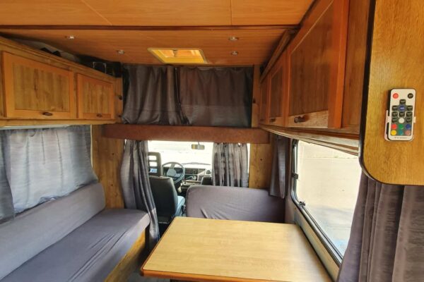 Innenansicht eines Wohnmobil mit Sitzbänken und Tisch.