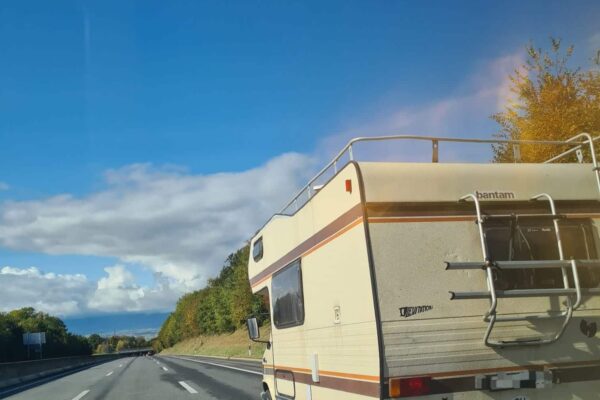 Wohnmobil fährt auf einer Autobahn unter blauem Himmel.