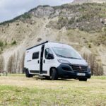 Van blanc garé devant une montagne rocheuse.