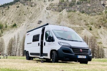 Van blanc garé devant une montagne rocheuse.