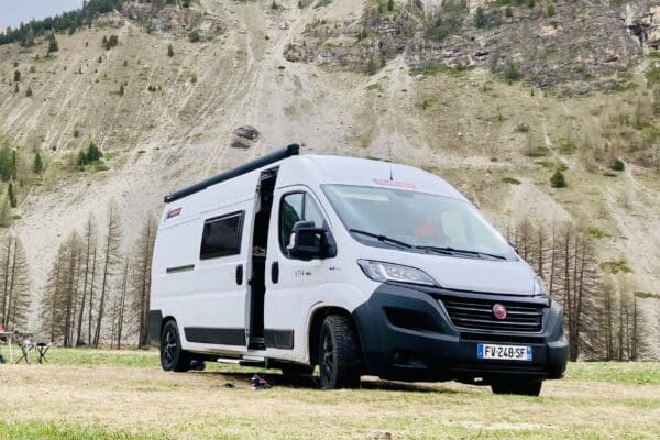 Van blanc garé devant une montagne rocheuse.