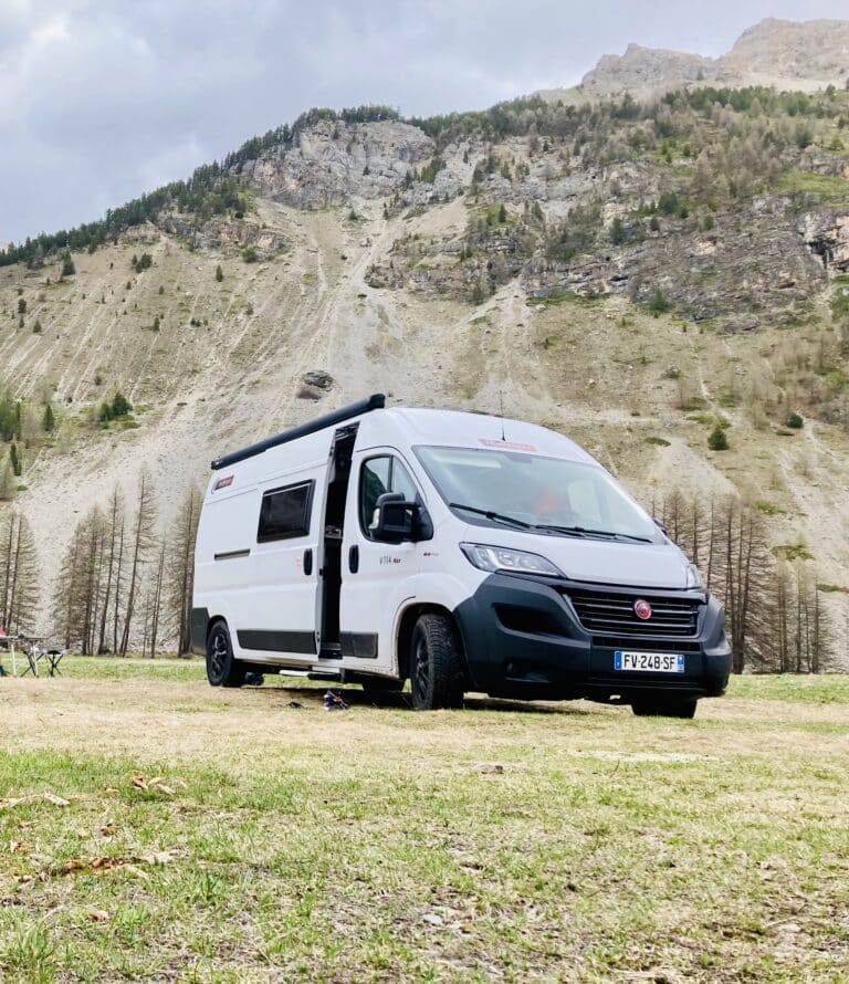 Van blanc garé devant une montagne rocheuse.