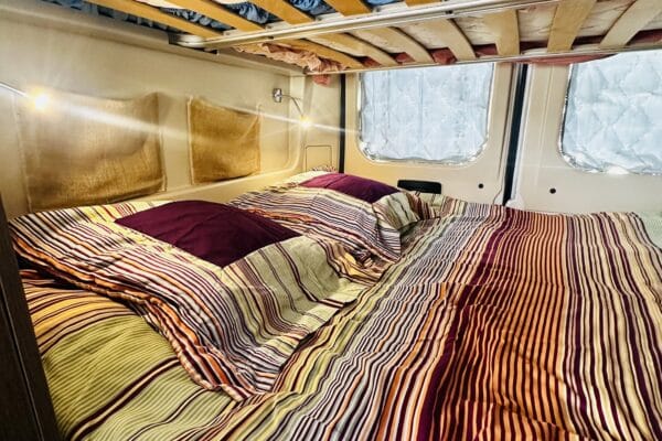 Kuscheliges Bett mit gestreifter Decke in einem Wohnmobil.