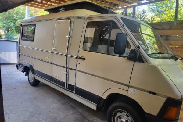Wohnmobil beige unter Holzschuppen geparkt.
