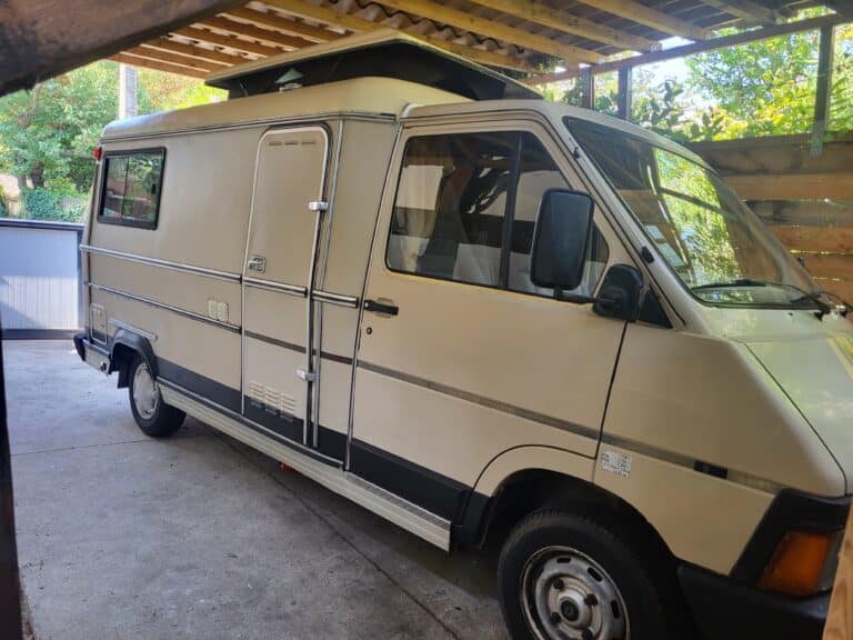 Camping-car beige garé sous abri en bois.