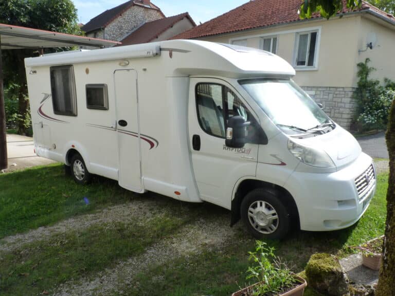 Camping-car blanc stationné devant maison