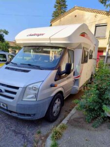 Camping-car blanc garé devant un bâtiment.