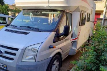 Camping-car blanc garé devant un bâtiment.
