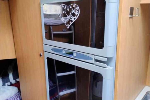 Réfrigérateur encastré dans une caravane, porte avec cœur décoratif.