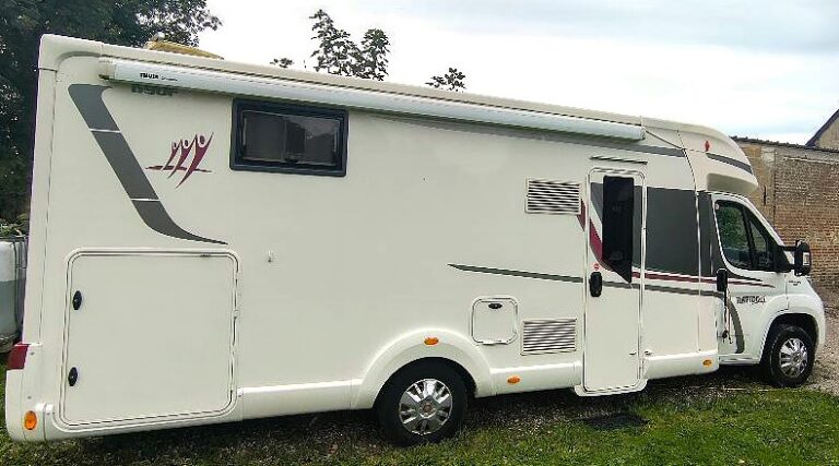 Camping-car blanc garé sur pelouse.