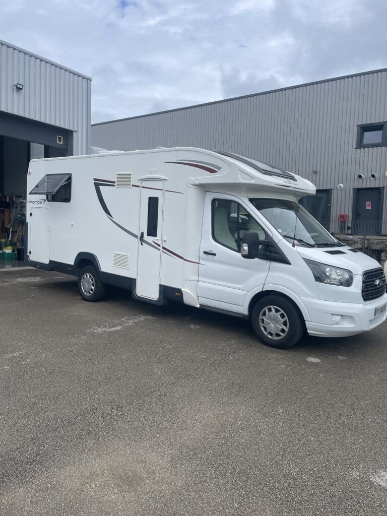 Camping-car blanc stationné devant un entrepôt.