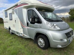 Camping-car garé sur l'herbe sous ciel nuageux.