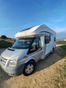 Camping-car blanc stationné sur chemin rocheux.