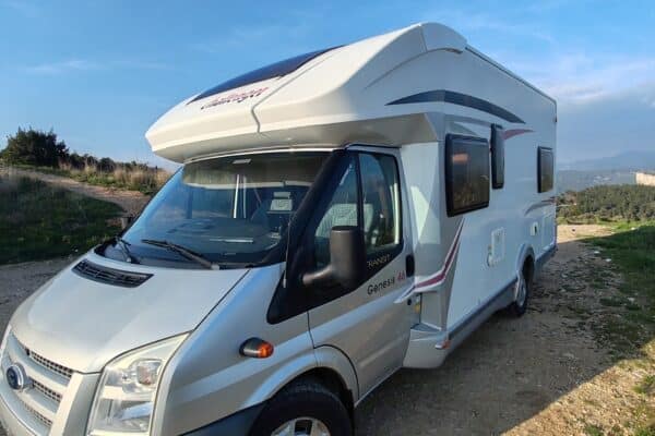 Camping-car blanc stationné sur chemin rocheux.