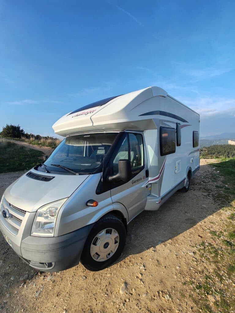 Camping-car blanc stationné sur chemin rocheux.