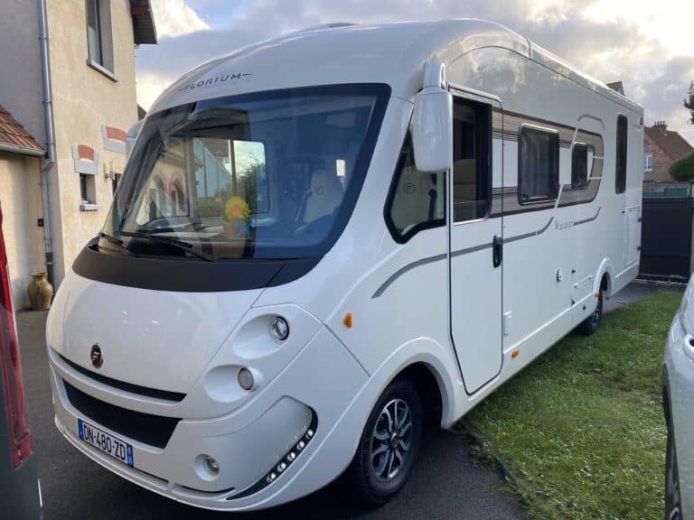 Camping-car blanc garé devant une maison.