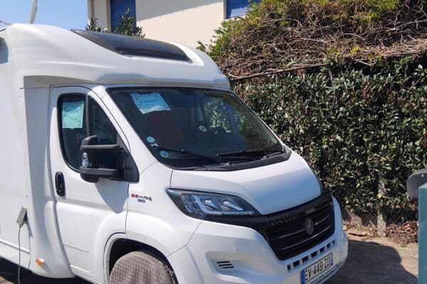Camping-car blanc stationné devant une maison.