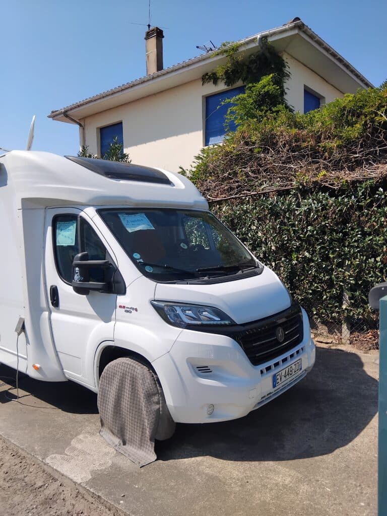Camping-car blanc stationné devant une maison.