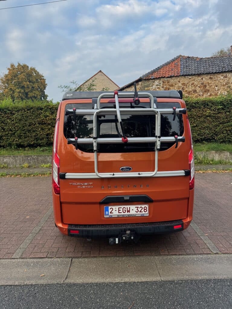 Fourgon orange avec porte-vélos à l'arrière.