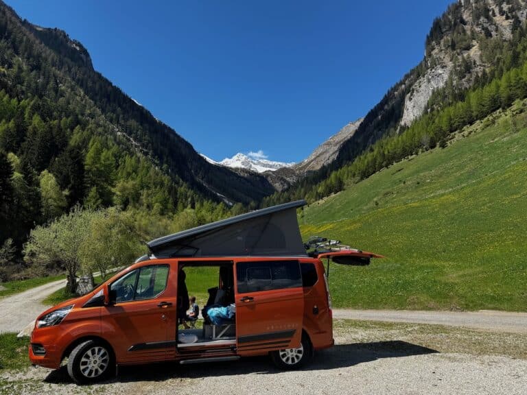 Van orange dans montagnes verdoyantes sous ciel bleu.