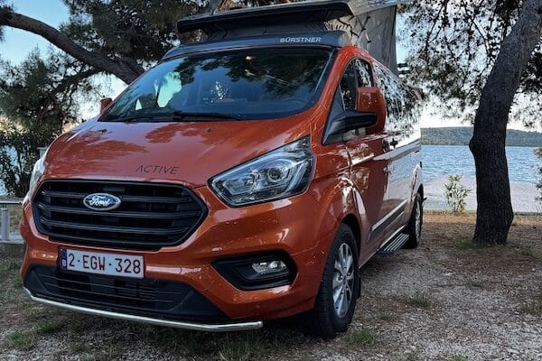 Van Ford orange près de la mer et des arbres.
