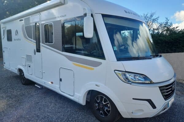 Camping-car blanc stationné sur une allée gravillonnée.