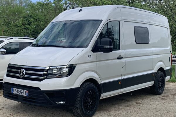 Fourgon blanc stationné sur un chemin bordé d'arbres.