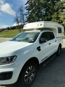 Camion pick-up blanc avec cellule campeur.