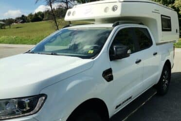 Camion pick-up blanc avec cellule campeur.