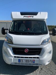 Camping-car blanc garé devant un bâtiment.