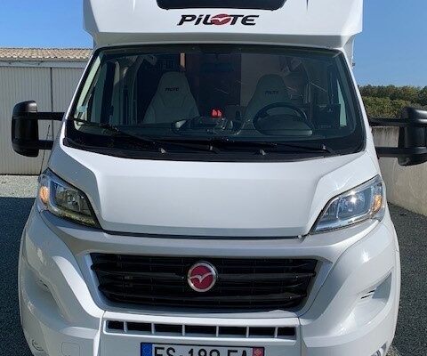 Camping-car blanc garé devant un bâtiment.