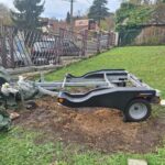 Remorque vide sur pelouse près de clôture.