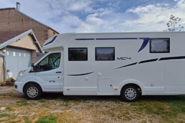 Camping-car blanc moderne garé devant une grange