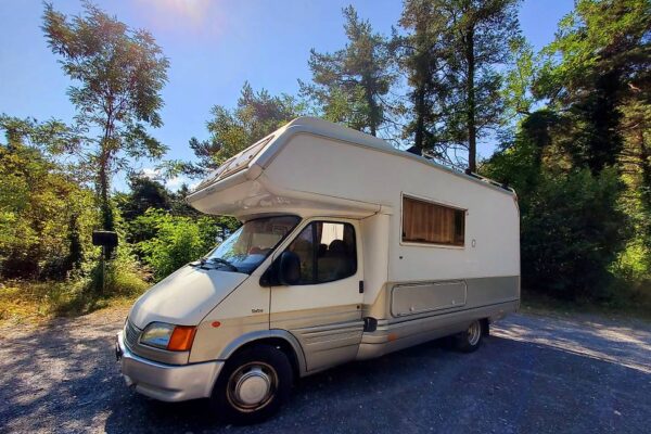 Camping-car blanc garé en forêt sous le soleil