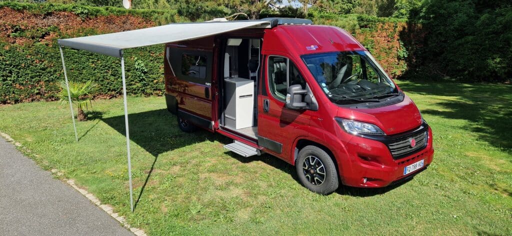 Camping-car rouge avec auvent ouvert sur herbe verte