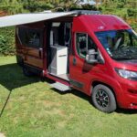 Camping-car rouge avec auvent ouvert sur herbe verte