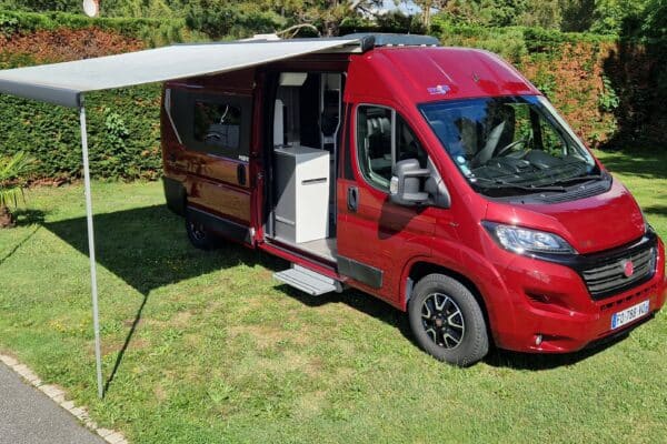Camper rosso con tenda aperta su erba verde