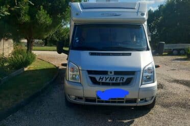 Camping-car Hymer garé entre arbres sous ciel bleu