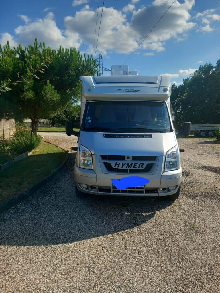 Camping-car Hymer garé entre arbres sous ciel bleu