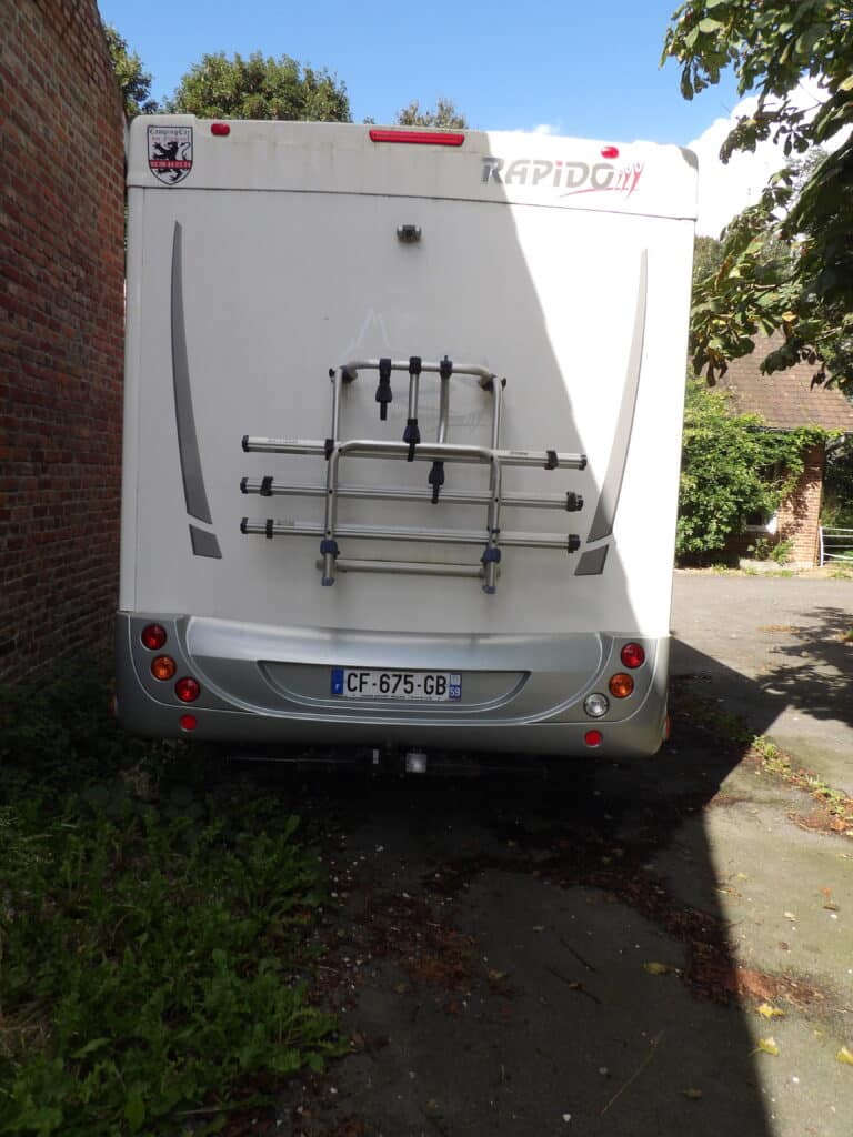 Camping-car blanc stationné, porte-vélos arrière, plaques d'immatriculation