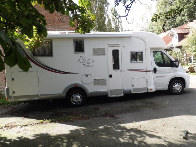 Camping-car blanc garé sous des arbres