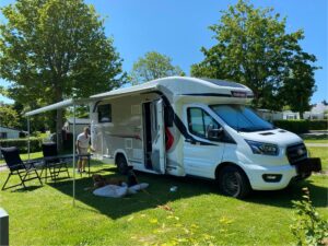Camping-car dans un parc verdoyant, homme et chien détendus.